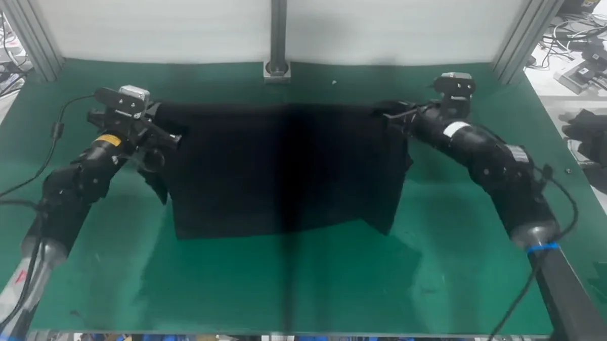 Official Griffin Labs video frame showing two robot arms folding a black shirt on a green tabletop.